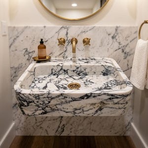 May include: A wall-mounted rectangular marble sink featuring prominent black veining on a white background. The sink includes a matching marble backsplash, brass faucet handles, a central brass spout, a brass drain, and a small brass soap dish.