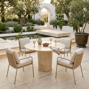 May include: Outdoor dining set featuring a round table with a light-colored stone base and top, surrounded by four chairs with woven backs and cream-colored cushions. The scene is set in a garden with a pool and olive trees.
