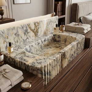 May include: A rectangular marble sink featuring a white base with prominent grey and gold veining. The exterior of the sink has a vertical fluted design. The basin is integrated into a matching marble countertop with a high backsplash.