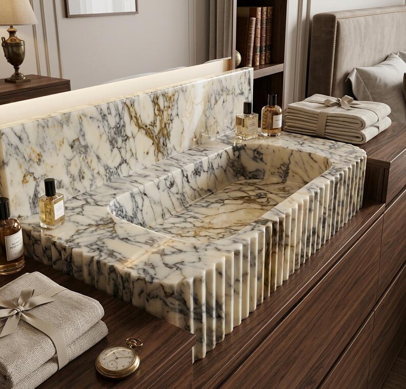 May include: A rectangular marble sink featuring a white base with prominent grey and gold veining. The exterior of the sink has a vertical fluted design. The basin is integrated into a matching marble countertop with a high backsplash.