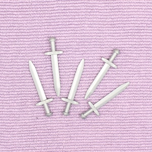 May include: Five silver toy swords arranged in a starburst pattern on a purple textured background.