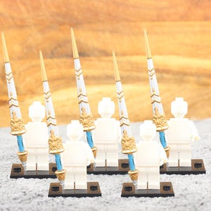 May include: Six white Lego minifigures holding gold and silver spears with blue accents. The figures are standing on black bases.