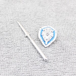 May include: A silver spear and shield set. The shield is blue with a silver lion's head emblem. The spear is silver with a pointed tip and a decorative handle. The set is likely a miniature collectible.