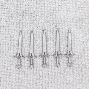 May include: Five silver-colored swords with intricate designs on a white textured background.