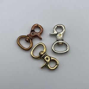 Pode incluir: Três fechos giratórios de metal em cobre, prata e latão. Cada fecho tem um gatilho com mola e um laço circular para fixação. Os fechos são projetados para uso com bolsas, chaveiros ou outros acessórios.