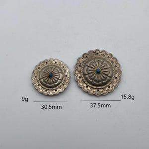 May include: Two silver-toned metal buttons with a turquoise center. The larger button is 37.5 mm in diameter and weighs 15.8 grams. The smaller button is 30.5 mm in diameter and weighs 9 grams.