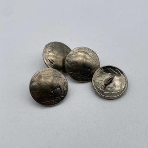 May include: Four silver-coloured buttons shaped like American five-cent coins featuring the profile of a buffalo. The buttons are arranged in a cluster on a white surface.