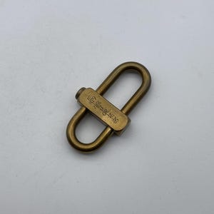May include: A gold-colored metal clasp with a rectangular tag that reads "The Little Things".