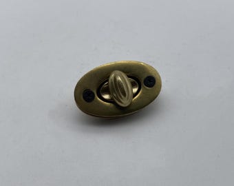 May include: A gold-toned oval-shaped metal clasp with a small, oval-shaped handle. The clasp has two small black screws on either side of the handle.