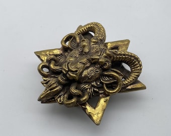 May include: A gold-toned metal brooch featuring a detailed sculpted ram's head with horns, set within a six-pointed star design.