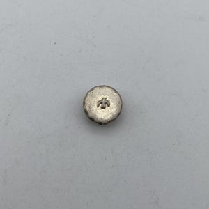 May include: A silver-coloured button with a raised design of a bird on the front.