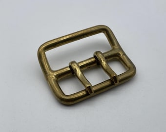 May include: A brass buckle with two prongs for a belt or strap.