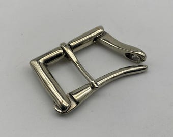May include: A silver metal belt buckle with a rectangular frame and a curved tongue. The buckle has a shiny finish. The design is simple and classic, suitable for various belt styles. The buckle is made of metal.