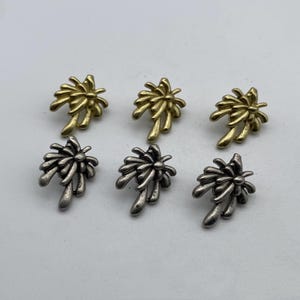 May include: Six palm tree shaped metal charms in two different finishes. Three are gold and three are silver.