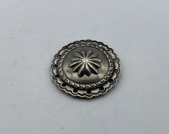 Może przedstawiać: Srebrny metalowy guzik z ozdobnym wzorem kwiatu w środku i falistym brzegiem.