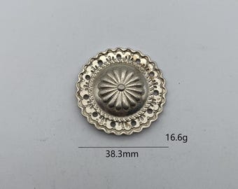 Może przedstawiać: Srebrny metalowy guzik z ozdobnym wzorem kwiatowym. Guzik ma średnicę 38,3 mm i waży 16,6 grama.