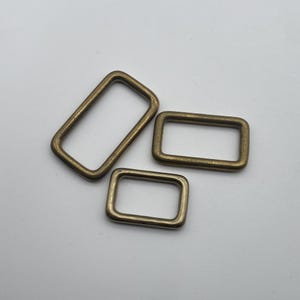 Peut inclure: Trois anneaux en D m&eacute;talliques dor&eacute;s de diff&eacute;rentes tailles. Les anneaux sont de forme rectangulaire et ont une finition lisse et polie.