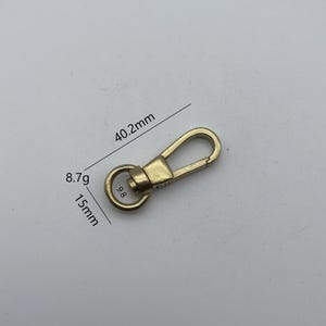 Puede incluir: Gancho giratorio de metal dorado con un anillo de 15 mm de diámetro y un gancho de 40,2 mm de largo. El gancho pesa 8,7 gramos.