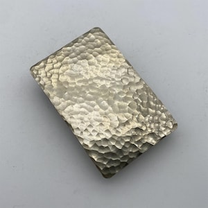 Puede incluir: Una hebilla rectangular de plata con textura martillada.
