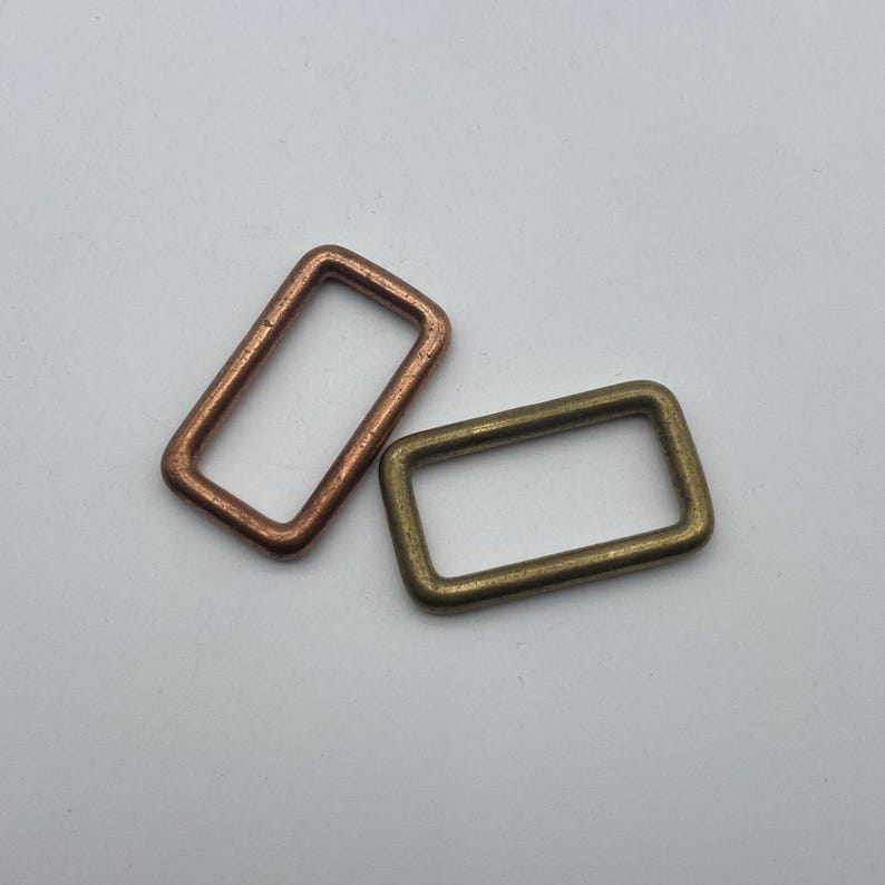 Peut inclure: Deux anneaux m&eacute;talliques, l'un en cuivre et l'autre en laiton, sont pr&eacute;sent&eacute;s sur un fond blanc. Les anneaux sont de forme rectangulaire et ont une finition lisse.