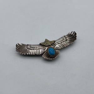 May include: Silver eagle pendant with turquoise stone and gold accents. The eagle is in flight with its wings spread wide.
