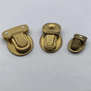 May include: Three gold-toned metal clasps of different sizes. The clasps have a rounded shape and a raised, ridged design.