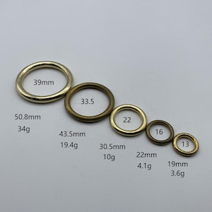 May include: A set of ten gold-toned metal rings of varying sizes. The rings are arranged in order of size, with the largest ring at the top and the smallest ring at the bottom. The rings are labeled with their diameter in millimeters and their weight in grams.