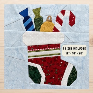 Könnte beinhalten: Ein Stoff-Quiltblock-Muster mit einem roten Weihnachtsstrumpf, gefüllt mit einem blau gestreiften Geschenk, einem grün gemusterten Geschenk, einer gelben Kugel und einer Zuckerstange. Der Text 3 SIZES INCLUDED 12" - 16" - 20" ist aufgedruckt.