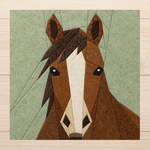 May include: A fabric quilt block featuring a pieced horse head design. The horse has a brown coat with a white blaze on its face, dark brown ears, and a dark brown mane. The background is a light sage green fabric with a subtle floral pattern.
