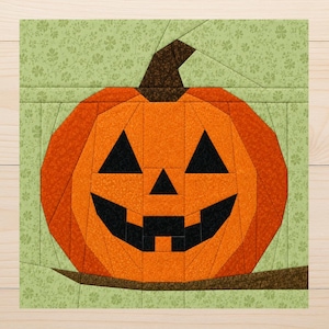 Puede incluir: Un bloque de tela cuadrado para acolchar con un diseño de calabaza de Halloween. La calabaza está construida con segmentos de tela naranja y ojos, nariz y boca de tela negra. Tiene un tallo marrón oscuro sobre un fondo verde claro con flores.