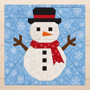 Könnte beinhalten: Ein quadratischer Stoff-Quiltblock mit einem zentralen Schneemann, der einen schwarzen Zylinder, einen roten Schal mit weißen Schneeflocken, eine orangefarbene Karottennase und drei schwarze Knöpfe trägt, vor einem hellblauen Hintergrund.