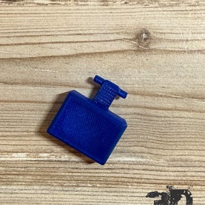 Op de afbeelding: Een klein, massief blauw rechthoekig object met een getextureerd oppervlak en een T-vormig uitsteeksel dat uit het midden van de bovenkant steekt. Het item heeft een duidelijk kruislings patroon over het hele oppervlak, typisch voor 3D-printen.