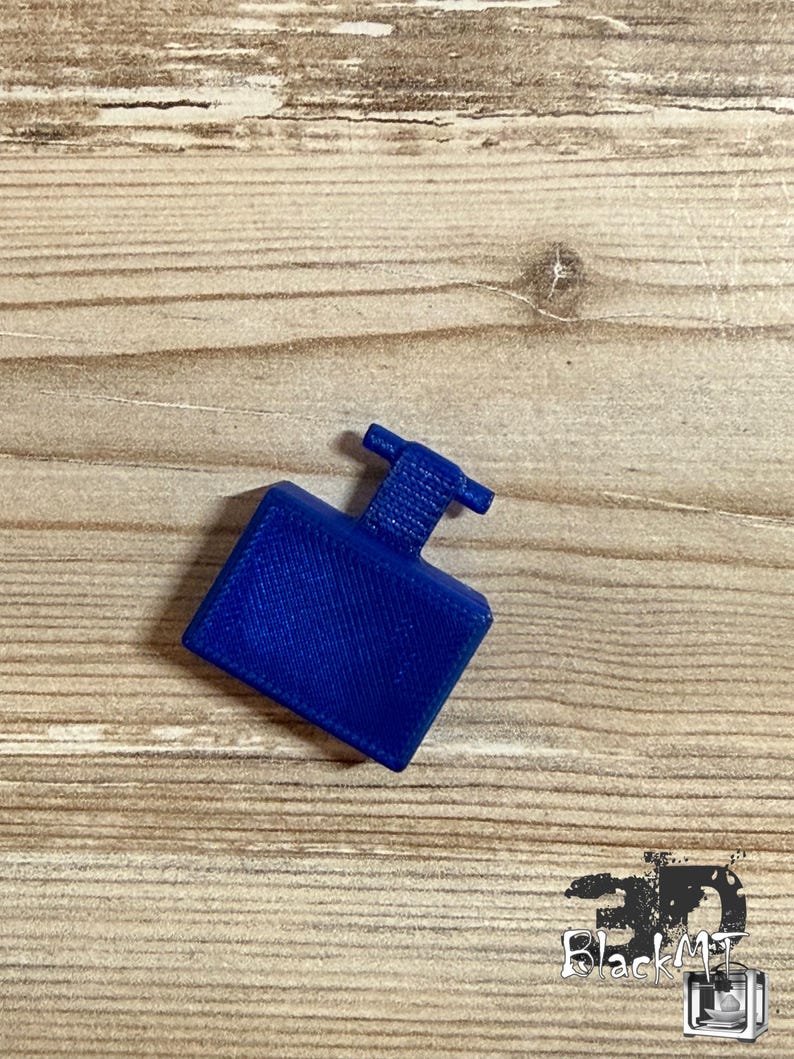 Op de afbeelding: Een klein, massief blauw rechthoekig object met een getextureerd oppervlak en een T-vormig uitsteeksel dat uit het midden van de bovenkant steekt. Het item heeft een duidelijk kruislings patroon over het hele oppervlak, typisch voor 3D-printen.