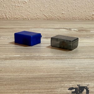 Op de afbeelding: Een rechthoekige blauwe plastic opbergdoos en een kleinere rechthoekige doorzichtige donkergrijze plastic opbergdoos. Beide containers hebben een eenvoudig ontwerp met een platte bovenkant en een scharnierend dekselmechanisme.
