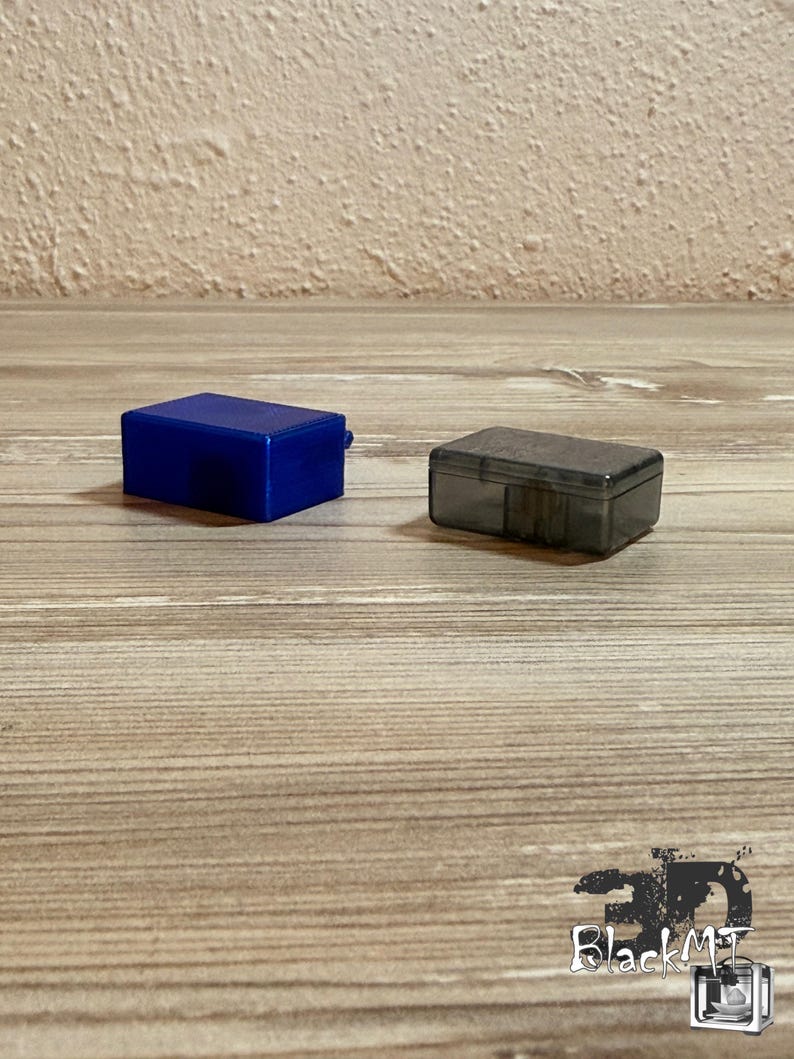 Op de afbeelding: Een rechthoekige blauwe plastic opbergdoos en een kleinere rechthoekige doorzichtige donkergrijze plastic opbergdoos. Beide containers hebben een eenvoudig ontwerp met een platte bovenkant en een scharnierend dekselmechanisme.