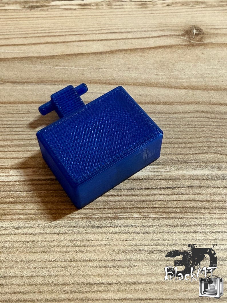 Op de afbeelding: Een rechthoekige, 3D-geprinte blauwe kunststof component met een getextureerde oppervlakteafwerking en een kleine, T-vormige uitstulping aan een van de zijden. Het object heeft een solide, doosachtige structuur met zichtbare lijnen van het printproces.