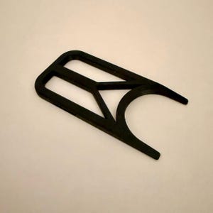 May include: A black, geometric tool with a rectangular handle and curved edges. The tool has a unique design with a central triangular cutout and two pointed ends, likely for a specific function.