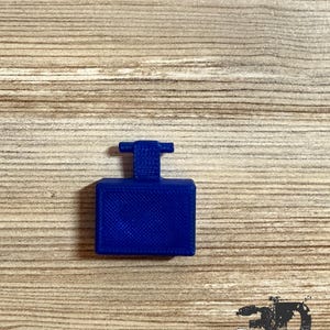 Op de afbeelding: Een kleine, rechthoekige component van koningsblauw plastic met een plat, getextureerd oppervlak en een verticaal lipje dat uit het midden van de bovenkant steekt. Het object heeft een 3D-geprinte afwerking met zichtbare kruispatronen.