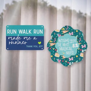 May include: Two decorative signs with text. The first is rectangular, teal and navy blue, with the words "RUN WALK RUN made me a runner" and "THANK YOU, JEFF." The second is flower-shaped, teal, with the words "WISHING YOU THE MOST MAGICAL MILES!"