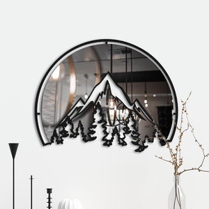 May include: A black metal wall mirror with a circular frame and a mountain silhouette design. The mirror reflects a room with a white ceiling and a light fixture.