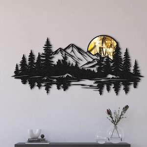 May include: Black metal wall art showing a mountain range, trees, and a lake with a yellow sun or moon. The artwork is mounted on a white wall above a wooden cabinet. The scene is a silhouette, suitable for home decor.