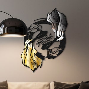 May include: Black and gold metal wall art featuring two stylized fish in a circular design. The art is mounted on a white wall above a beige couch with black pillows.