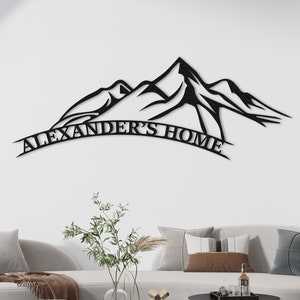 Puede incluir: Arte de pared de metal negro con una silueta de cordillera de montañas con el texto "Alexander's Home" en una pancarta curva debajo.