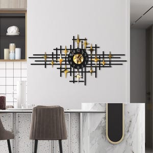 May include: A contemporary kitchen interior with a black and gold geometric wall clock. Two brown, upholstered bar stools with black legs and gold detailing are positioned in front of a marble countertop. Kitchen cabinets and appliances are also visible.