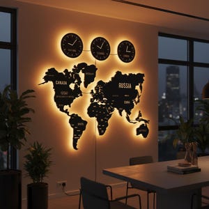 Op de afbeelding: Een zwarte wereldkaart wandkunst met verlichte randen, met drie klokken erboven die tijdzones voor New York, Istanbul en Londen aangeven. De kaart bevat landlabels zoals Canada, Rusland en Brazilië. De wandkunst is op een lichtgekleurde muur gemonteerd.