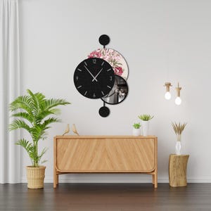 May include: A modern wall clock with a black face and white hands, set against a floral patterned circle and a mirrored circle. The clock is suspended from a black circular element. The overall design is contemporary and decorative.