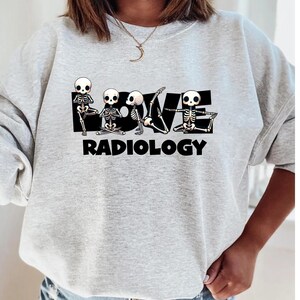 Może przedstawiać: Szara bluza z nadrukiem szkieletów w pozach jogi, które tworzą słowo "LOVE" z tekstem "RADIOLOGY" poniżej.