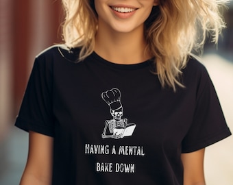 May include: Black t-shirt with a white graphic of a skeleton wearing a chef's hat and reading a cookbook. The text "HAVING A MENTAL BAKE DOWN" is printed below the graphic.