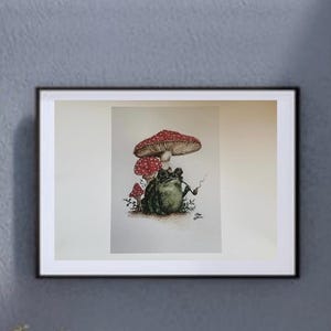 May include: Framed art print depicting a green frog smoking a pipe, under three red and white spotted mushrooms. The artwork is set against a white background within a black frame, suitable for wall decor. The image has a whimsical style.