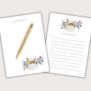 May include: Two white notepads with floral illustrations and a gold pen. One notepad has a to-do list. The illustrations include red flowers, blue flowers, and a bucket with the text "MARCHE AUX FLEURS". The name "ELIZA HOLBROOK" is printed on both notepads.